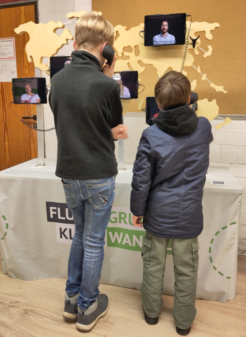 Zwei Schüler hören Interviews von Menschen, die aus Klimagründen fliehen mussten